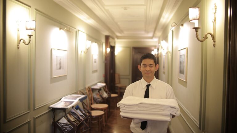 A hotel staff member carrying fresh linen along a corridor, part of the back-of-house movement hotels depend on